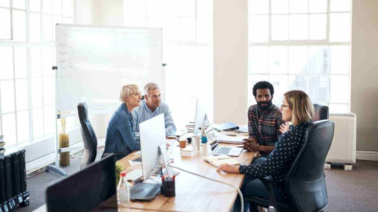Group of professionals in a meeting room discussing strategies, representing collaboration and learning in a Business Administration Course.