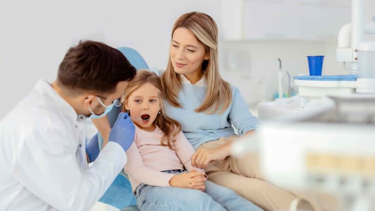 Dentist examining a young girl’s teeth while her mother provides comfort at Allina Health Richfield Clinic.