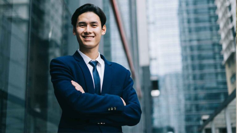 Confident young professional wearing a black business suit mens, standing outdoors in a modern cityscape.