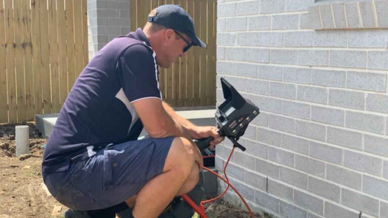 Technician using a gully camera for drain inspection outside a building.