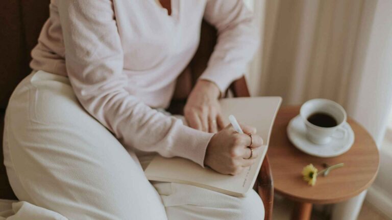 Woman writing notes beside a cup of coffee – illustrating the relaxing morning routine for the best coffee weight loss recipe.