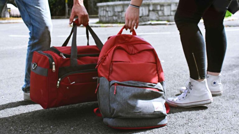 Two travelers holding an Allpa 35L travel pack and duffel bag on the road