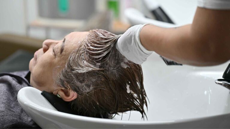 Person getting hair treatment at a salon, showing how Batiste Dry Shampoo Travel Size keeps hair clean and fresh without washing.