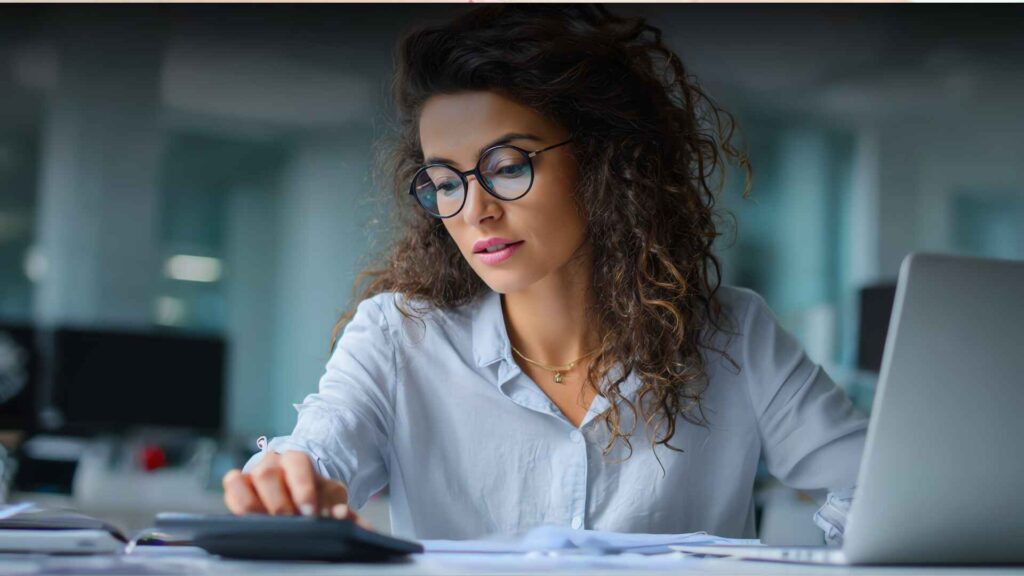 Professional woman using accounting software for multiple businesses on laptop and calculator in modern office.