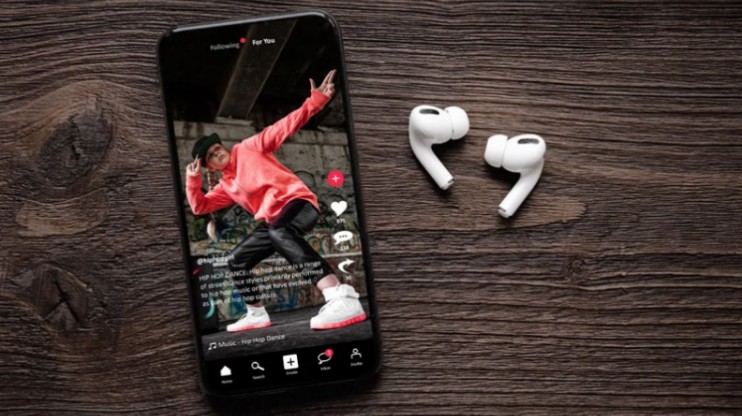 Best Tiktok Viewer Guide To Watch Content Anonymously TikTok viewer app on smartphone showing dance video with wireless earbuds on wooden table