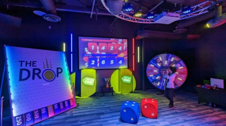 Game Show Battle Rooms That Take Team Fun To New Levels Contestant playing in a vibrant Game Show Battle Room featuring “The Drop” board, prize wheel, and interactive team challenges.